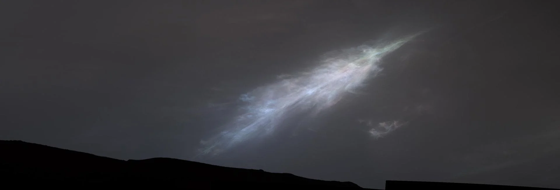 A glowing white light in a dark night sky with a silhouetted landscape below.